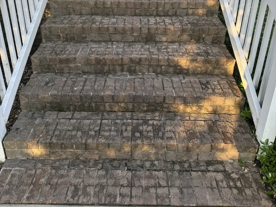Dark, stained brick front steps with white railings before cleaning