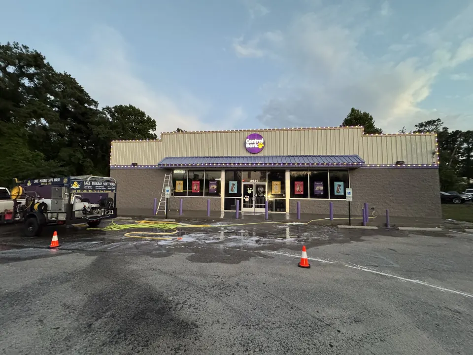 Storefront and parking lot being cleaned, with the Lake Murray Soft Wash trailer, cones and a ladder