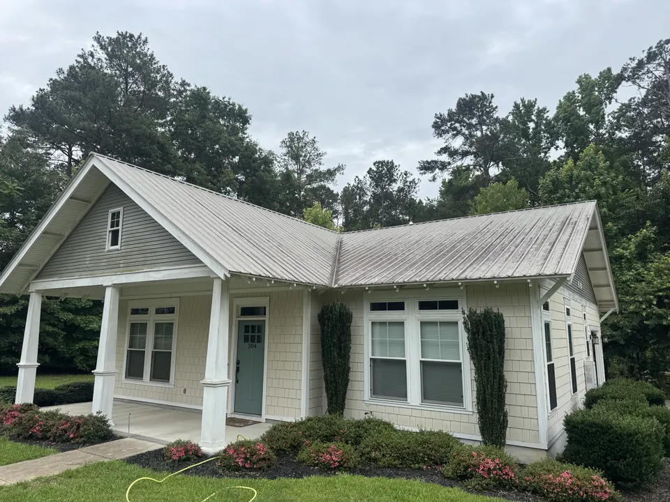 Cottage with a streaked metal roof and dingy siding before cleaning