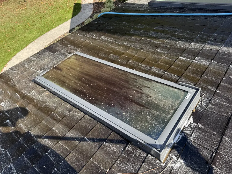 Skylight on an asphalt shingle roof with dirty, streaked glass before cleaning